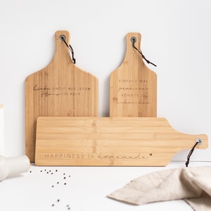 Könnte beinhalten: Drei Holz-Schneidebretter mit gravierten Sprüchen. Das obere Brett sagt "Liebe macht aus jedem Haus ein Heim". Das mittlere Brett sagt "Einfach mal probieren konnte ja schmecken". Das untere Brett sagt "Happiness is homemade".
