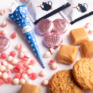 May include: A variety of sweet treats including pink and white candy, chocolate-filled cones, pink foil-wrapped chocolates, and shortbread cookies. The treats are arranged on a white surface.