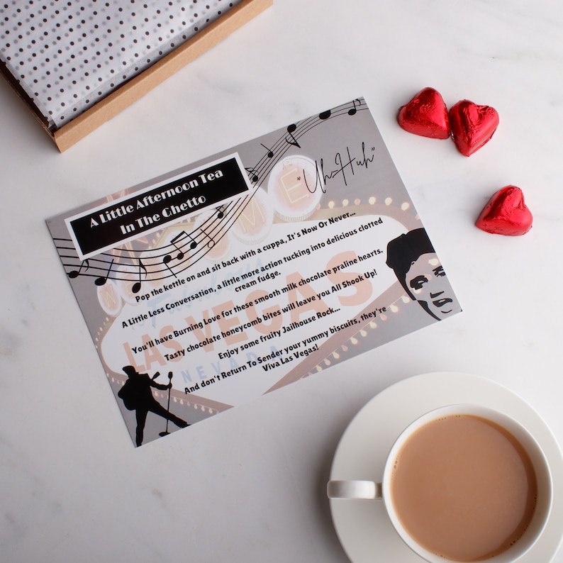 May include: A grey card with a musical note design and the text "A Little Afternoon Tea In The Chetto" and "Viva Las Vegas!"  The card also features a black and white illustration of a person singing into a microphone.  There are three red heart-shaped chocolates on a white surface.
