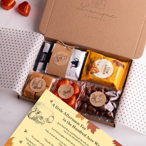 May include: A brown cardboard box filled with a variety of treats, including chocolate, biscuits, and tea. The box is decorated with a Winnie the Pooh theme and the text "A little Afternoon Tea in the Hundred Acre Wood".