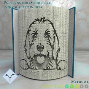 Può includere: Un libro con un volto di cane intagliato nelle pagine. Il libro aperto mostra l'immagine del cane. Il testo in alto recita "PATTERNS FOR 28 BOOK SIZES 16 IN CM + 12 IN INCHES". Il libro ha copertine blu ed è su una superficie bianca.