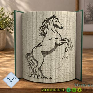 May include: A book sculpture featuring a folded page design that creates a silhouette of a rearing horse. The book has dark green covers and is displayed open, showcasing the intricate paper folding technique used to form the equine image.