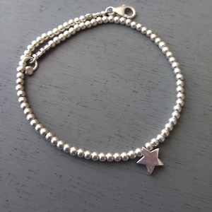 May include: A silver beaded bracelet with a star charm. The bracelet is made of small, round beads and has a simple, elegant design.