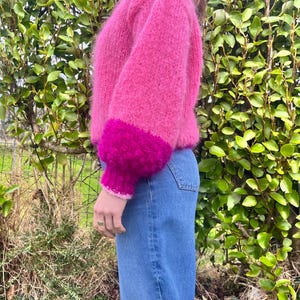 Peut inclure: Un pull rose vif &agrave; col montant et manches longues. Les poignets sont d'une nuance de rose plus fonc&eacute;e, cr&eacute;ant un effet color-block. Le pull est associ&eacute; &agrave; un jean bleu, offrant un look d&eacute;contract&eacute; et &eacute;l&eacute;gant.