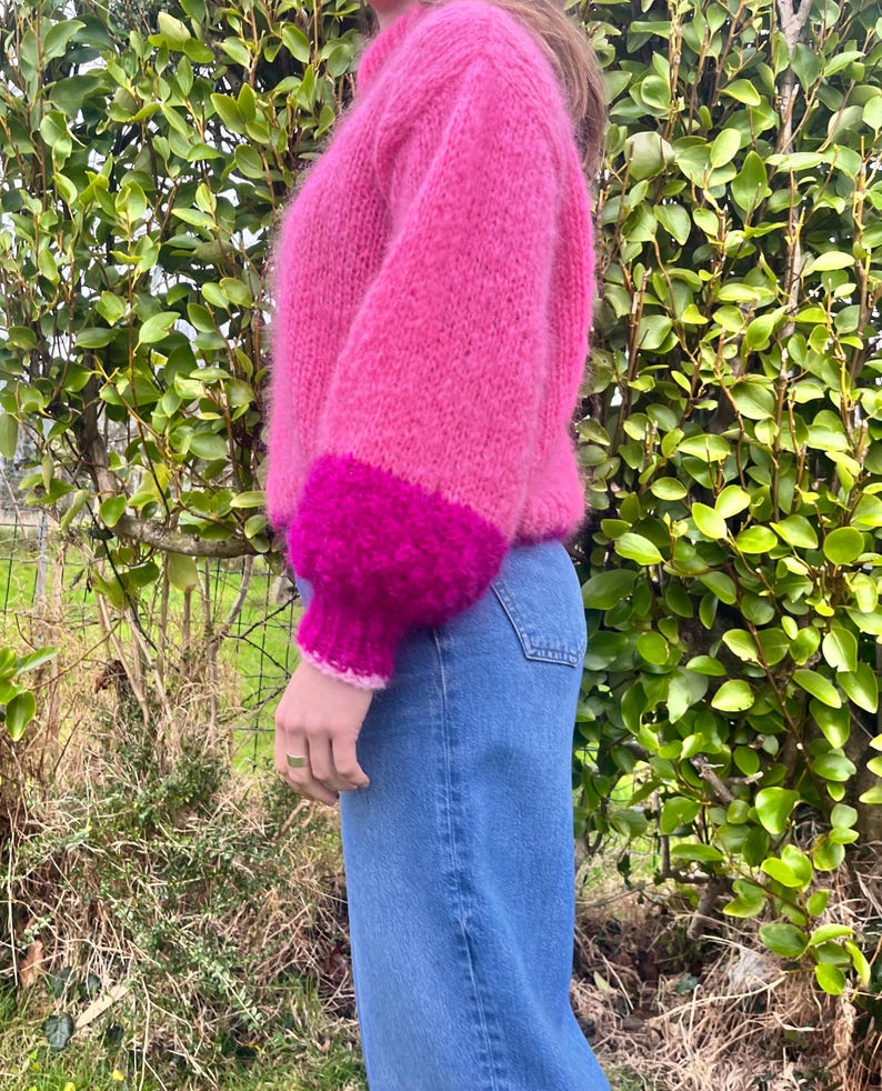 Peut inclure: Un pull rose vif &agrave; col montant et manches longues. Les poignets sont d'une nuance de rose plus fonc&eacute;e, cr&eacute;ant un effet color-block. Le pull est associ&eacute; &agrave; un jean bleu, offrant un look d&eacute;contract&eacute; et &eacute;l&eacute;gant.