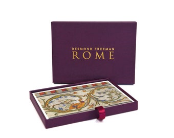 May include: A purple box with a gold inscription that reads "DESMOND FREEMAN ROME". The box is open and a card with a colorful mosaic design is visible inside.