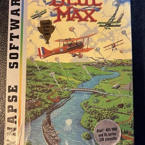 May include: A vintage "Blue Max" video game box. The box art features biplanes in a dogfight over a landscape with a river and a battleship. The text includes "SYNAPSE SOFTWARE", "Game of the Year 1984", and "Atari 400/800 and XL series 32K cassette".