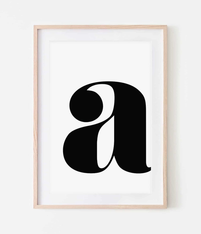 May include: A black and white printable art print featuring the letter 'a' in a bold, stylized font. The letter is centered on a white background and framed in a light wood frame.