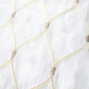 May include: Close-up of white fabric with a woven, net-like pattern. The pattern is created with cream-colored yarn and tan-colored accents. The fabric has a slightly textured appearance.