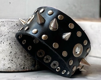 Brazalete ancho de cuero negro con pinchos / Pulsera con tachuelas, conos y ojales plateados / Accesorio alternativo