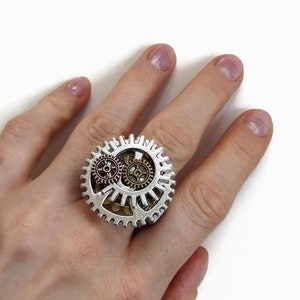 May include: A silver ring with three interlocking gears. The gears are in different sizes and have a copper, gold, and silver finish.