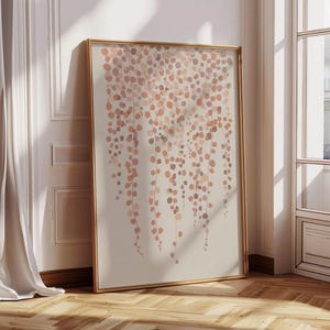 Op de afbeelding: Een ingelijste kunstdruk met een beige achtergrond, met een patroon van afdalende, cirkelvormige vormen in perzik- en bruintinten. Het kunstwerk zit in een goudkleurige lijst en leunt tegen een witte muur.