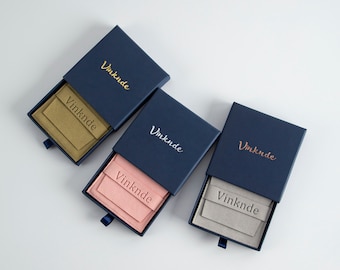 May include: Three navy blue boxes with the word "Vinknde" printed on the top. Each box contains a smaller box with a different colour lining: beige, pink, and grey.