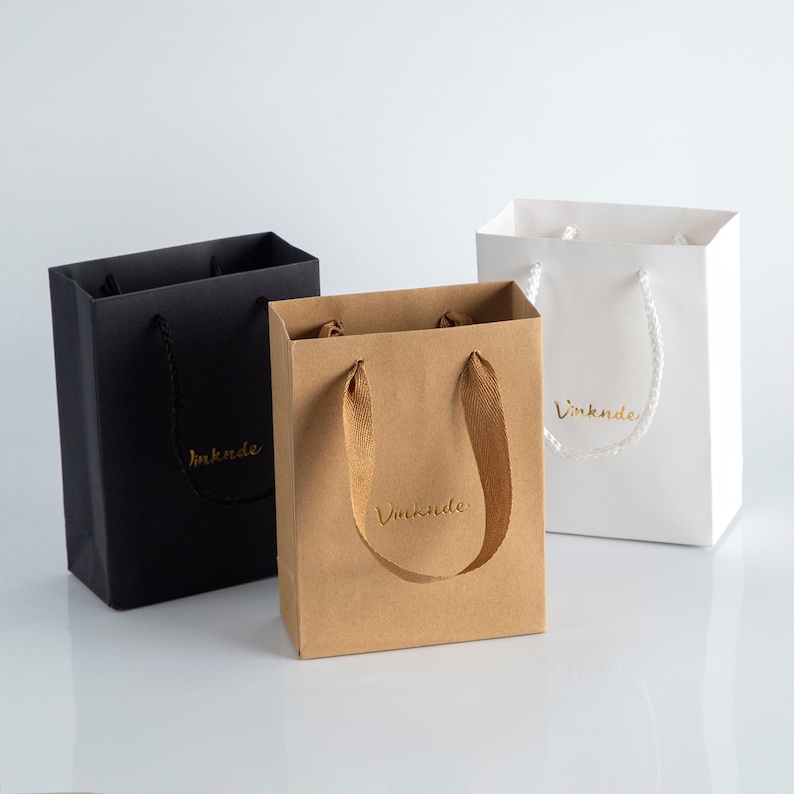 May include: Three small gift bags with handles. The bags are black, brown, and white. Each bag has the word "Vinknde" printed on the front in gold lettering.