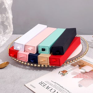 May include: Assortment of small, rectangular boxes with sliding drawers. The boxes are in various colors, including white, pink, light blue, black, and red.