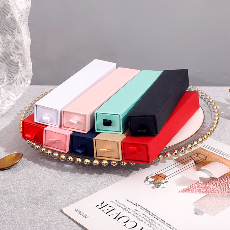 May include: Assortment of small, rectangular boxes with sliding drawers. The boxes are in various colors, including white, pink, light blue, black, and red.