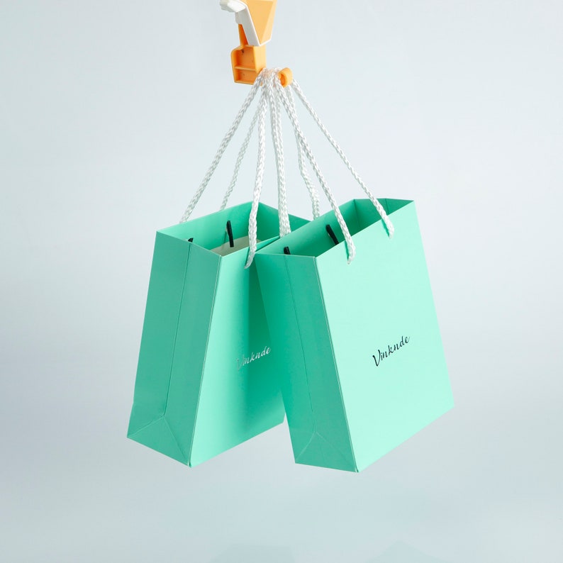 May include: Two turquoise blue paper gift bags with white handles and the word "Vunkunde" printed on the front.