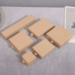 May include: Set of six brown cardboard boxes with drawer pulls. The boxes are arranged in a size gradient, with the largest box at the top and the smallest box at the bottom.