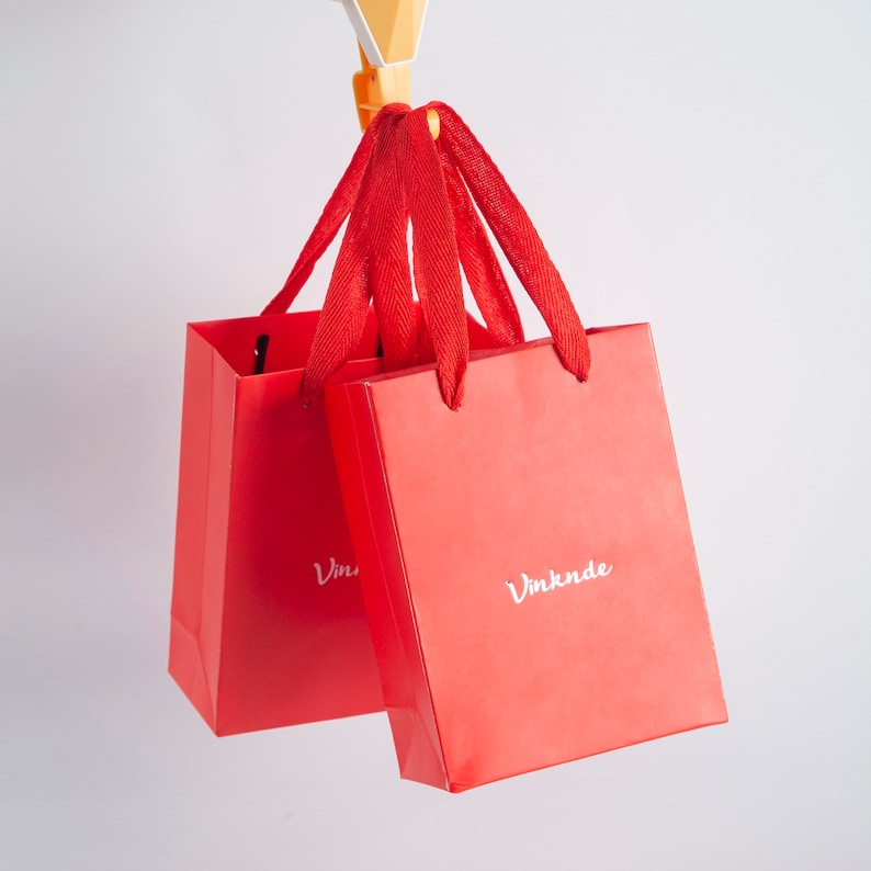 May include: Two red shopping bags with white text. The bag on the left says "Vin" and the bag on the right says "Vmknde".