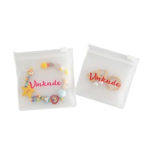 Puede incluir: Dos bolsas de pl&aacute;stico transparente con cierre de cremallera con la palabra "Vinknde" impresa en rosa en cada bolsa. Una bolsa contiene un brazalete de cuentas de colores con un dije de estrella y la otra bolsa contiene un anillo de oro y un pendiente de perla.