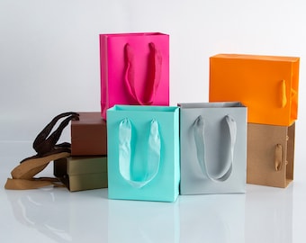 May include: Five colorful paper gift bags with handles. The bags are stacked on top of each other. The bags are pink, blue, gray, orange, and brown.