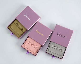 May include: Three open rectangular gift boxes in a row, each with a different coloured interior. The boxes are a light purple with the word "Vinknde" printed on the top. The interior colours are tan, pink, and grey.