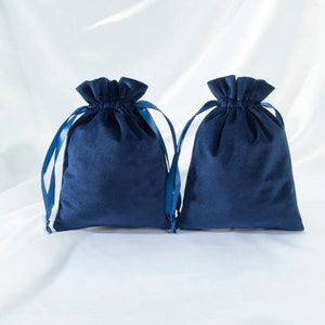 Pode incluir: Duas bolsas de cord&atilde;o de veludo azul com la&ccedil;os de fita de cetim azul combinando. As bolsas est&atilde;o colocadas sobre uma superf&iacute;cie branca.