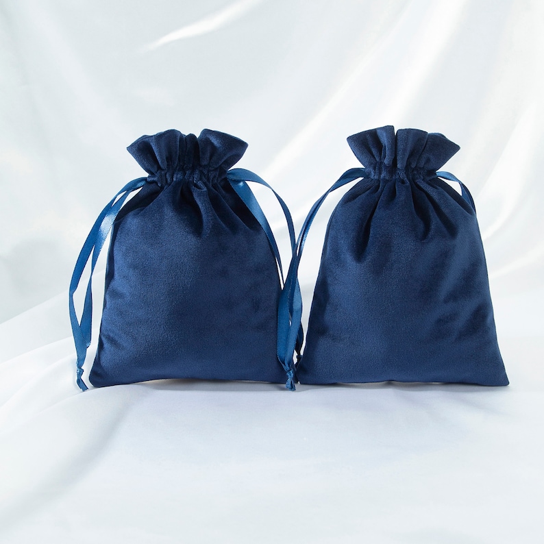 Pode incluir: Duas bolsas de cord&atilde;o de veludo azul com la&ccedil;os de fita de cetim azul combinando. As bolsas est&atilde;o colocadas sobre uma superf&iacute;cie branca.