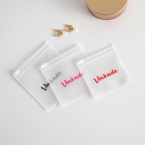 Puede incluir: Tres bolsas de pl&aacute;stico transparentes con cremallera con la palabra "Vinknde" impresa en negro, rosa y rojo.