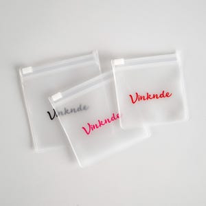 Puede incluir: Tres bolsas de pl&aacute;stico transparentes con cremallera, con la palabra "Vinknde" impresa en negro y rojo en la parte delantera.