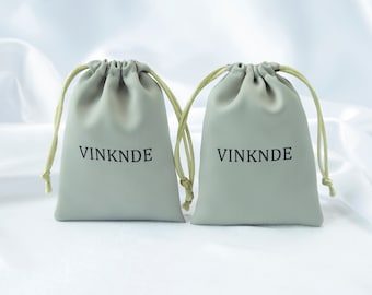 Op de afbeelding: Twee lichtgrijze trekkoordzakjes met het woord "VINKNDE" in het zwart op de voorkant.