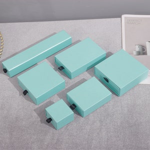 May include: Five light blue gift boxes with black pull tabs. The boxes are arranged in a size order from largest to smallest.