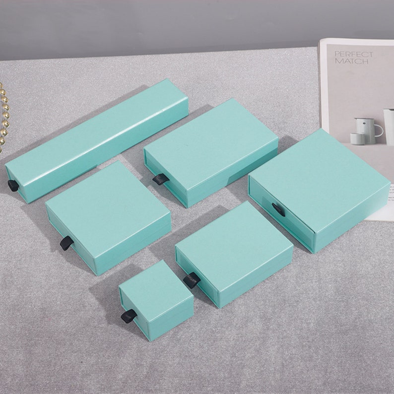 May include: Five light blue gift boxes with black pull tabs. The boxes are arranged in a size order from largest to smallest.