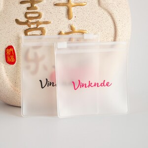 Puede incluir: Dos bolsas de pl&aacute;stico transparentes con cierre de cremallera, con la palabra "Vinknde" impresa en rosa en una bolsa y "Vin" impresa en negro en la otra bolsa.