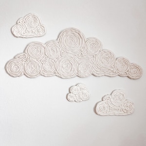 May include: Four white clouds made of rope, each with a different size and shape, are arranged on a white wall. The clouds are made of rope that is twisted into circles.