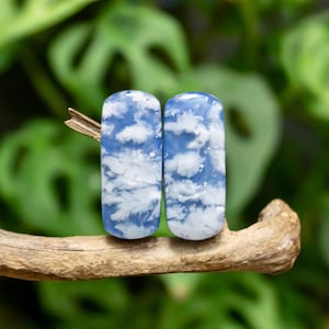 May include: Two rectangular cabochons with a smooth, polished surface featuring a sky blue base color and irregular white cloud-like patterns. The stones are positioned side-by-side, displaying a consistent color palette and a glossy finish.