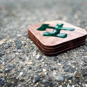 May include: A set of four wooden coasters with a green resin inlay in the shape of the letter "H".