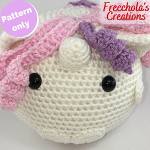 Può includere: Testa di unicorno all'uncinetto con dettagli rosa, viola e bianchi. L'unicorno ha occhi neri a bottone e un corno bianco. Il testo "Pattern only" è in un cerchio rosa e "Frecchola's Creations" è visibile.