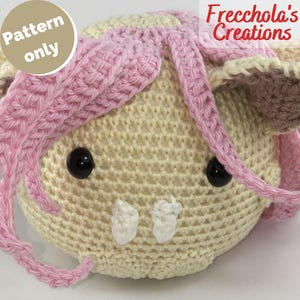 May include: A crocheted bunny head pattern in cream and pink yarn. The bunny features black button eyes and white teeth. The text "Pattern only" is in a circle on the left. The text "Frecchola's Creations" is on the right.