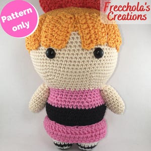 Può includere: Bambola all'uncinetto fatta a mano raffigurante Blossom delle Superchicche. La bambola presenta un viso e un corpo color crema, capelli arancioni, un fiocco rosso e un vestito rosa e nero. Il testo "Pattern only" e "Frecchola's Creations" sono visibili.