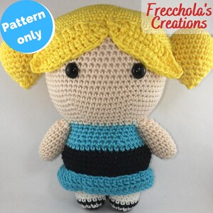 Può includere: Bambola all'uncinetto fatta a mano che assomiglia a un personaggio dei cartoni animati, con codini gialli, occhi neri a bottone e un vestito blu e nero. La bambola ha il testo "Pattern only" e "Frecchola's Creations".