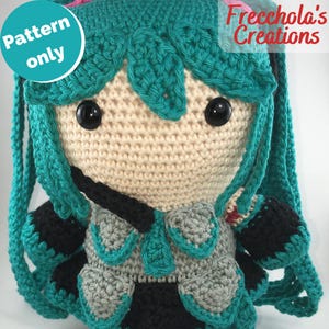 May include: A crocheted doll with teal hair and accents, black eyes, and a cream-colored face. The doll has a gray and black outfit with teal details. The image includes the text "Pattern only" and "Freechola's Creations".