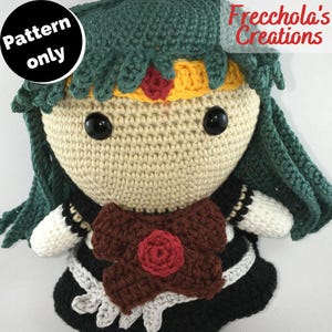 Può includere: Bambola amigurumi all'uncinetto con capelli verdi, un fiocco marrone e un vestito bianco e nero. La bambola ha una fascia gialla e rossa. La bambola è solo un modello, non un prodotto finito. "Frecchola's Creations" è scritto nell'angolo in alto a destra dell'immagine.