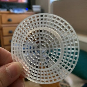 May include: A white plastic circular loom with a grid pattern. The loom is designed for creating circular crocheted projects.