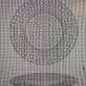 May include: A silver-colored metal circular object with a grid pattern. The object has a smaller circular opening in the center. The object is casting a shadow on a surface below.