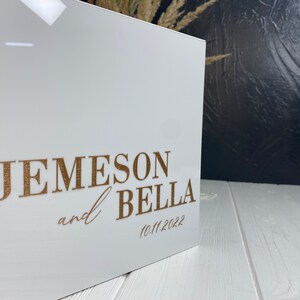 Op de afbeelding: Witte acrylbox met gouden opschrift "Jemeson en Bella 10.11.2022".