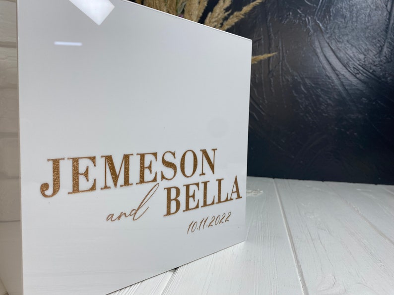 Op de afbeelding: Witte acrylbox met gouden opschrift "Jemeson en Bella 10.11.2022".