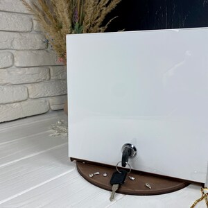 Op de afbeelding: Witte doos met een sleutelgat en een sleutel in het sleutelgat. De doos staat op een houten basis met een paar decoratieve stukken.