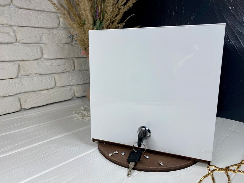 Op de afbeelding: Witte doos met een sleutelgat en een sleutel in het sleutelgat. De doos staat op een houten basis met een paar decoratieve stukken.