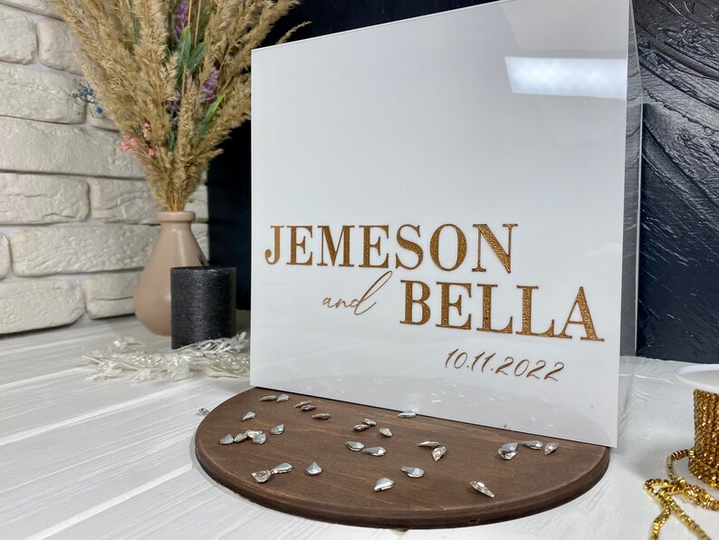 Op de afbeelding: Witte acrylbox met gouden opschrift "Jemeson en Bella 10.11.2022".